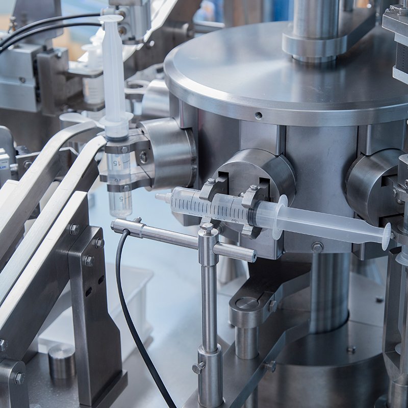 Robotic syringe filling machine performing automated liquid filling and capping under sterile conditions.