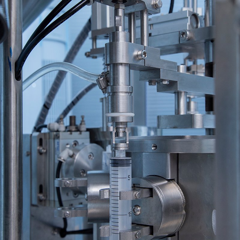 Internal mechanism of a syringe filling machine showing nozzles and capping heads.